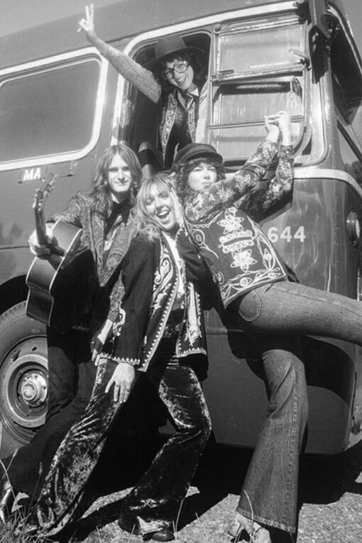 A group of hippie friends posing in front of vintage cars in the 1960s