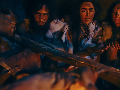 Neanderthal and Homo sapiens families gather around a bonfire in a prehistoric cave, wearing animal skins, cooking and enjoying meat, depicting the ancient lifestyle of hunter-gatherer tribes during a night feast