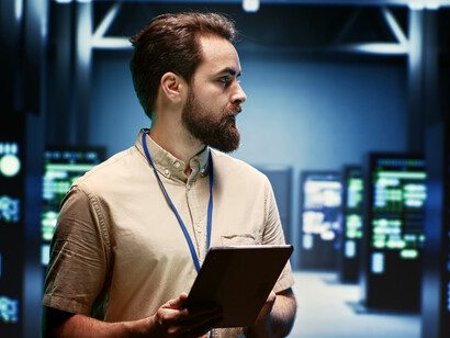 A data center server room showing a technician inspecting racks of physical computing infrastructure