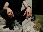 A person sitting on a step with a can and a cigarette 