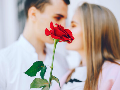 A rose held delicately as a couple shares a moment behind it, highlighting romance, drama, and the stakes of reality dating shows like Bachelor