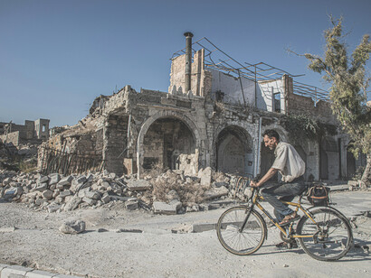 Idlib, Idlib Governorate, Syria. An unrecognizable biker rides past demolished houses in a landscape marked by the destruction of war