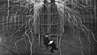 A glow of nitrogen fills the atmosphere as Nikola Tesla is photographed sitting in front of his generator in 1899