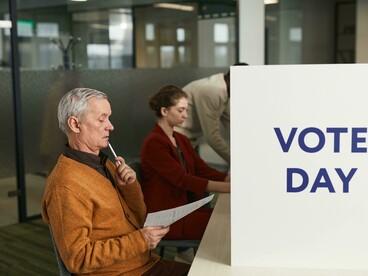 A man in a brown sweater stands near a polling place on voting day as people cast their ballots