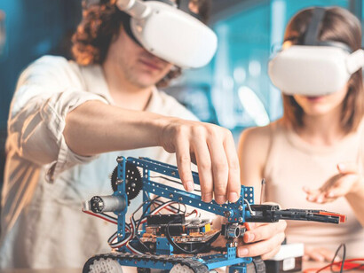 Young man and woman wearing VR glasses conducting robotics experiments in a laboratory with robots and tools
