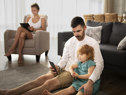 Parents and their child share the same living room, yet remain disconnected, each focused on their mobile phones