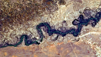 The Syr Darya River floodplain appears here as a maze of winding meanders and loops at the image’s center. The darkest areas mark dense brush along the river’s current course, filled with blue-green water, while lighter wisps of vegetation trace the swampy depressions, or sloughs, that flank it