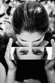 A woman stares into the camera through a mirror held in her hands