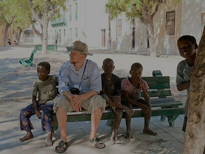 Turista sentado na praça com crianças locais, Ilha de Moçambique, Nampula, Moçambique