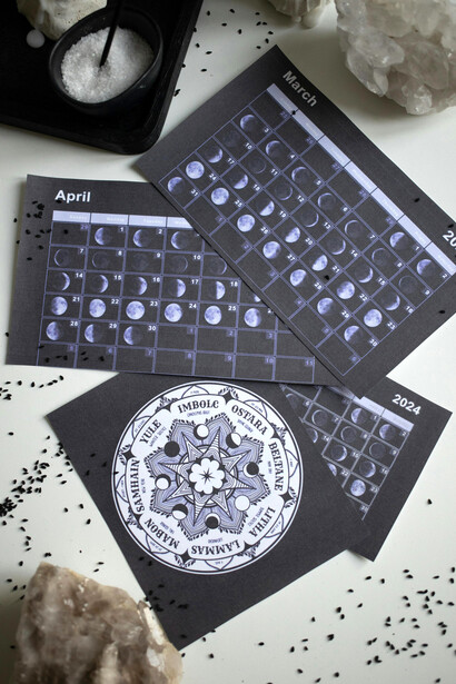 A Wheel of the Year chart and calendar laid out on a white desk, symbolizing the cyclical rhythm of time and seasons