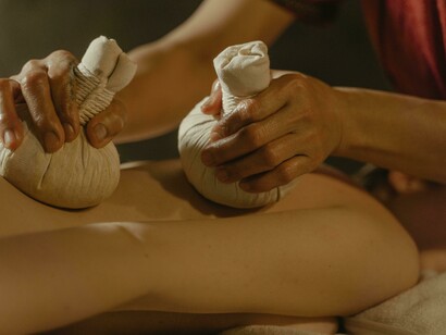 A practitioner’s hands massaging a person’s bare back with herbal fabric balls, illustrating a traditional Panchakarma therapy technique