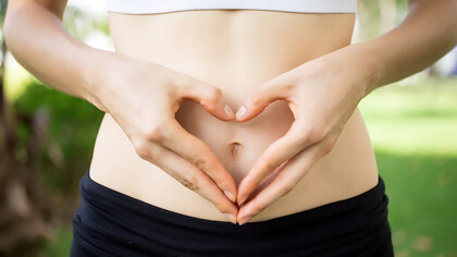 Close-up of female hands forming a heart shape on her belly, symbolizing improved gut health and well-being