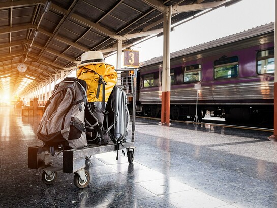 Bagagens aguardam ao lado de um trem em uma estação iluminada pelos primeiros raios de sol. A imagem representa o momento concreto da partida, enquanto a ansiedade pré-viagem muitas vezes começa muito antes, ainda no espaço íntimo de casa