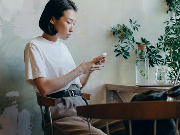 A woman in a white shirt sits alone in a cozy café, talking on the phone