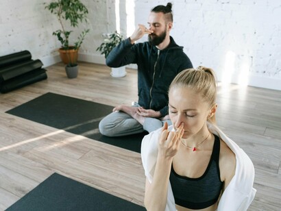 A woman and a man sit in meditation, eyes gently closed, creating a tranquil atmosphere, a mindful exercise that promotes focus and attentiveness, crucial for staying committed to personal and professional goals
