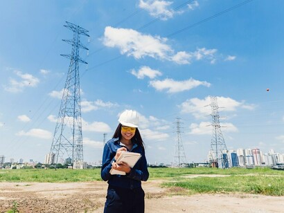 Wearing a safety helmet, a woman takes detailed notes while examining a high-voltage line, addressing critical issues of energy efficiency in the context of the ongoing energy crisis