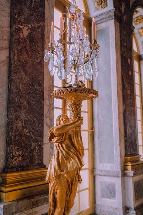 A golden statue with a candle holder illuminates the lavish interiors of the Palace of Versailles, showcasing the palace's regal elegance