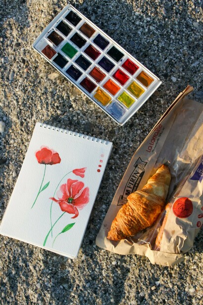 Aquarelas, caderno de desenhos e um croissant acompanham um momento de contemplação antes de novos desenhos. A viagem torna-se também um exercício de observação sensível e de criatividade
