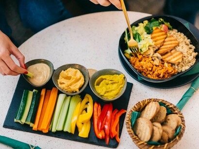 Na foto aparece as mãos de duas pessoas comendo alimentos feitos a partir de produtos de origem vegetal