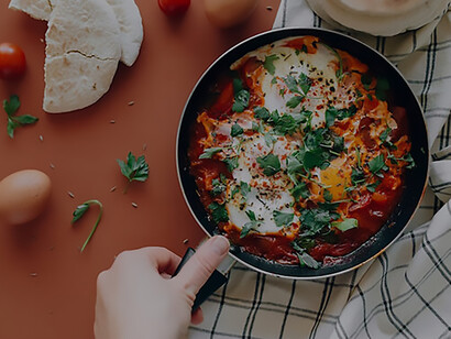 
In the heart of the frame lies a captivating image – a steaming pan filled with the savory allure of shakshuka, set against the backdrop of a carefully arranged table
