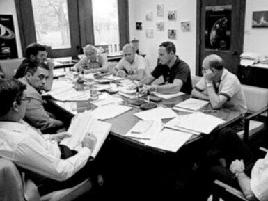 Centre spatial Johnson, 1982, à Houston, au Texas, États-Unis. Autour d’une table de débriefing, les astronautes des missions STS-2, STS-3 et STS-4 partagent leurs retours de vol. Au premier plan, John W. Young consigne les échanges, témoin attentif d’une nouvelle ère du programme spatial américain