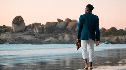 A businessman walks barefoot along the beach at sunset, carrying his shoes as he embraces a moment of peace, freedom, and reflection by the ocean