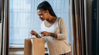 Mulher direciona olhar faminto para dentro de sacola de comida que pediu por aplicativo de delivery