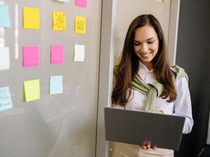 A businesswoman holds a laptop as she leads a presentation and guides her mentee during a team discussion