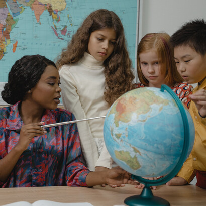 Professora mostra continentes no globo para alunos do ensino fundamental 2