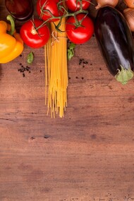 A table showing an assorted selection of food, including pasta, tomatoes, eggplants, bell peppers, onions, basil, olives and bread