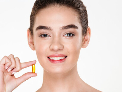 Beauty portrait of a smiling, healthy woman with dark hair holding a multivitamin capsule