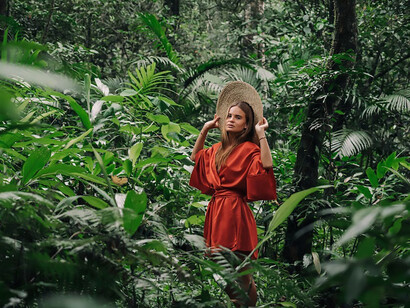 Embraced by the lush forests of Bali, Indonesia, a woman in a striking red dress ventures alone, weaving through the verdant beauty with a sense of tranquil independence