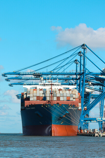 Under a clear blue sky, a cargo ship glides across the sea, making its way to a bustling harbor in China