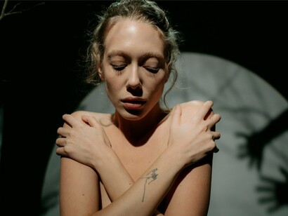 A vulnerable figure wrapped in her own arms, reflecting the emotional impact of harsh self-judgment