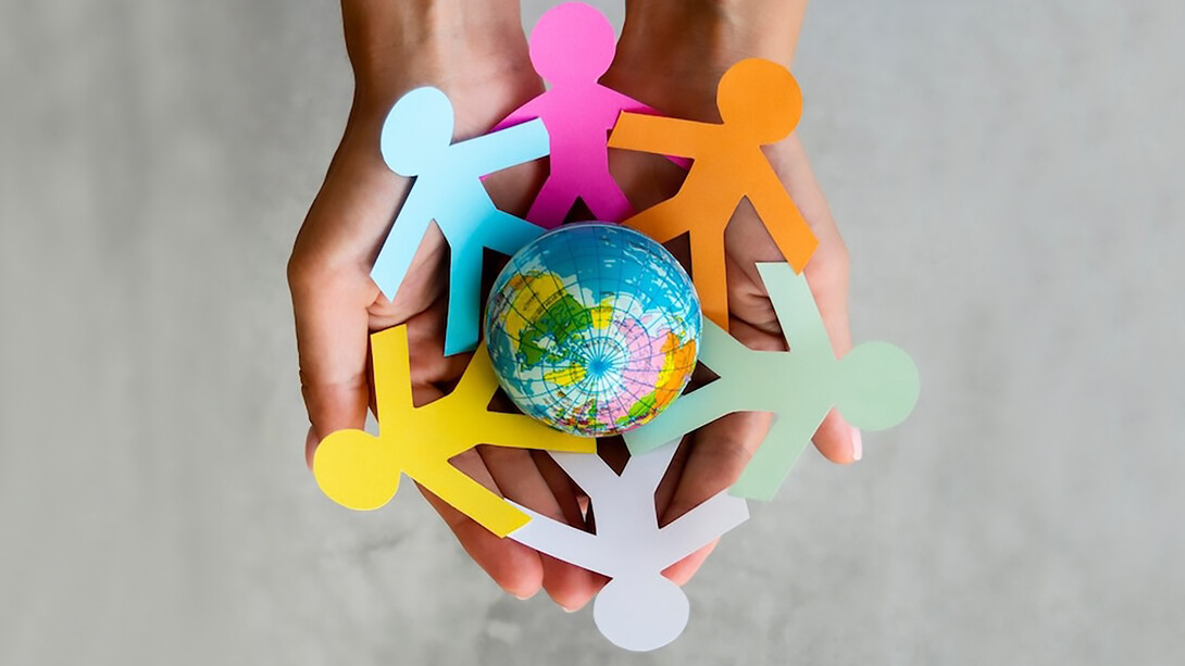 A top-view image of interconnected origami people forming a chain around the globe, symbolizing unity, peace, and vibrant diversity with an array of colors