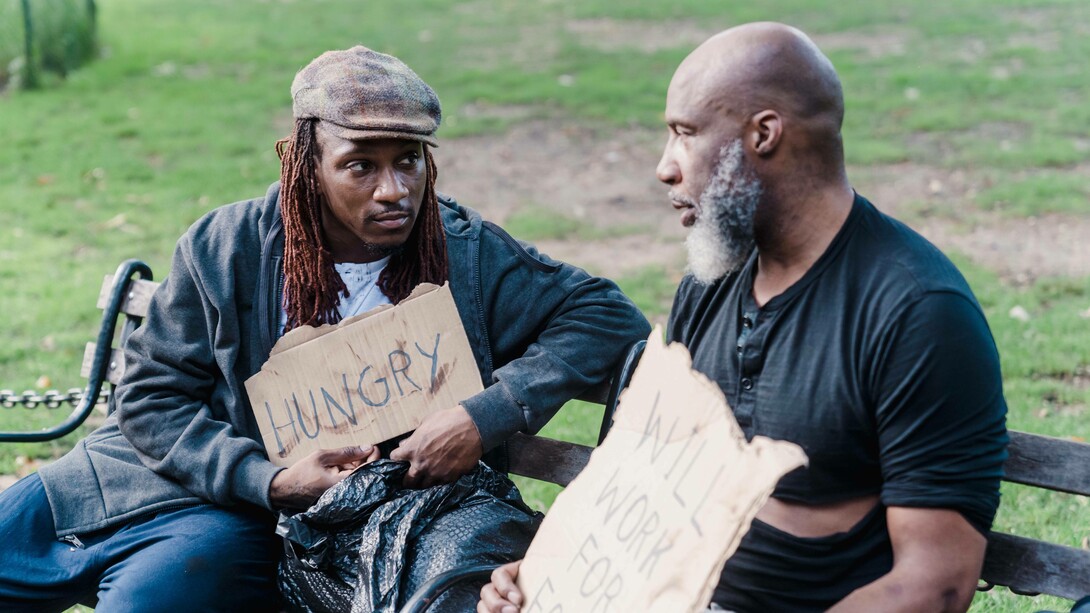 Two men hold signs that indicate poverty