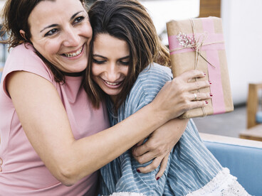 A daughter gives a gift and hugs her mother on the sofa for Mother’s Day