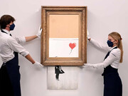 Gallery employees pose with Love is in the Bin by Banksy, photo by Facundo Arrizabalaga/EPA