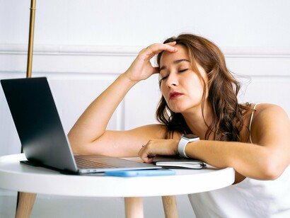 A weary employee pausing at her desk with her eyes closed, reflecting the mental strain that can accompany financial worries at work