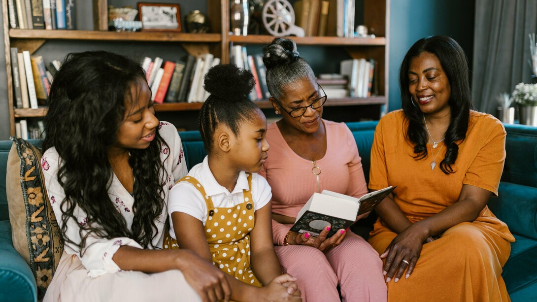 A grandmother reading a story to her daughters and grandchild, representing the passing of memory, wisdom, and culture across generations