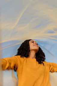 A woman stands in an open field, holding a flowing cloth that dances with the wind, symbolizing freedom and connection to nature