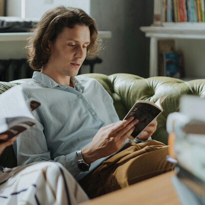 Joven con sentado en un sillón verde, leyendo junto a alguien. La esencia de ser no se puede captar con conceptos ni fórmulas, pero se puede adquirir en las experiencias
