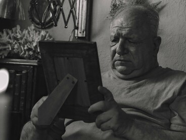 Homem segura um porta-retrato enquanto observa a fotografia com expressão de saudade. As lembranças de quem amamos continuam presentes mesmo quando precisamos aprender a conviver com a ausência