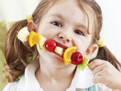 Una niña comiendo una brocheta de fruta