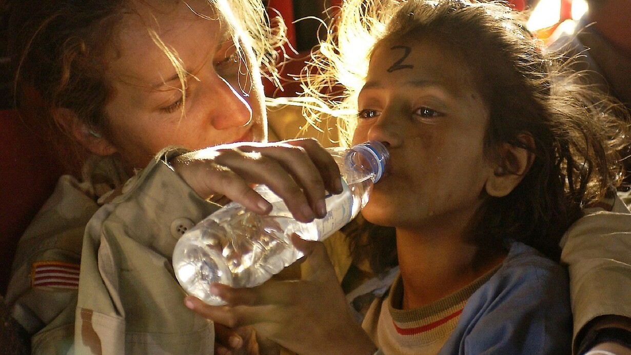 Soldier gives a drink of water to a child refugee
