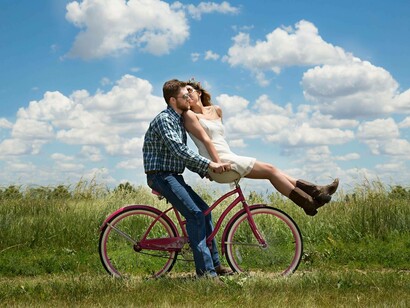 A couple riding a bicycle in a field on a sunny day displaying happiness to one another