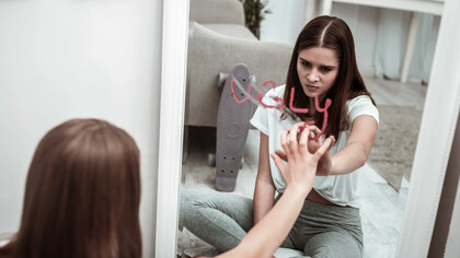 A teenage girl looks at the word ugly in a mirror