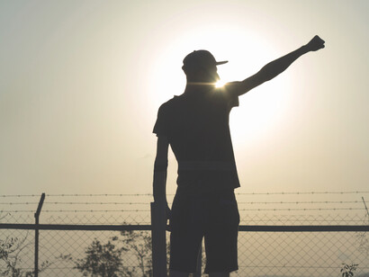 A young man holds his hand up against the sun in confidence