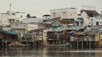 L'image présente des habitations traditionnelles sur pilotis en bordure d'un cours d'eau, typiques des paysages fluviaux du delta du Mékong au Vietnam