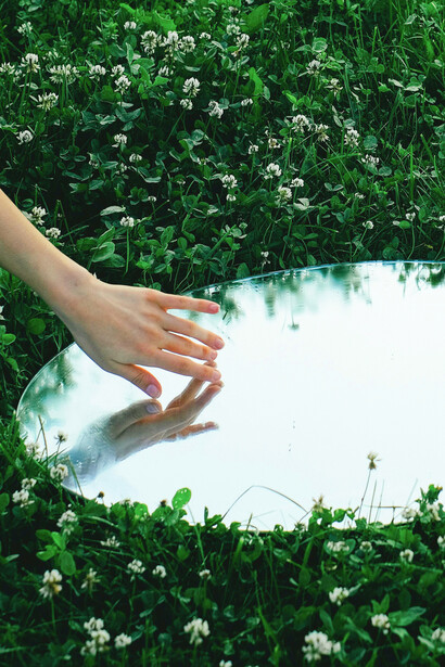 The touch of her hand on the mirror’s surface hints at the delicate balance between self-exploration and the external pressures of curated identities in today’s media